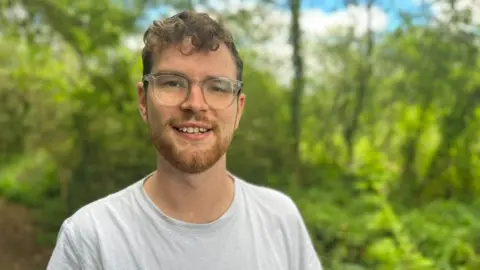 Sibling Support Callum Fairhurst, in Salhouse Broad woodland, wearing spectacles and a cream-T-shirt