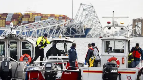 Rescue workers on boats are pictured with the bridge and ship in the background in Baltimore on 26 March