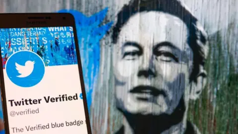 Getty Images Twitter Verified icon seen on mobile screen with Elon Musk in the background