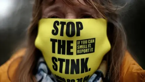 Reuters A woman wears a "Stop the Stink" face mask during a protest outside the gates of Walleys Quarry landfill in Silverdale