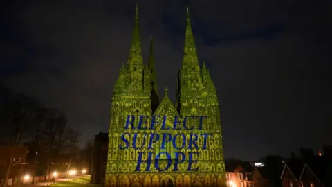Getty Images Lichfield Cathedral is illuminated in yellow light, with the words 'Reflect', 'Support', and 'Hope'.