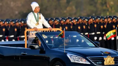 Getty Images Myanmar's military chief Min Aung Hlaing stands in a car as he oversees a military display at a parade ground to mark the country's Independence Day in Naypyidaw on January 4, 2023.