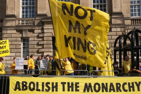 PA Media Protesters wave a large yellow flag with the words 'Not my king' and another banner fixed to barriers which reads 'Abolish the monarchy'