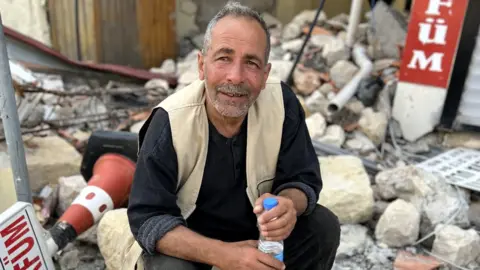 Wietske Burema/BBC Ibrahim Sener, pictured sitting among the rubble outside a shop in Antakya