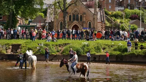 PA Media Horses in River Eden while crowd watches