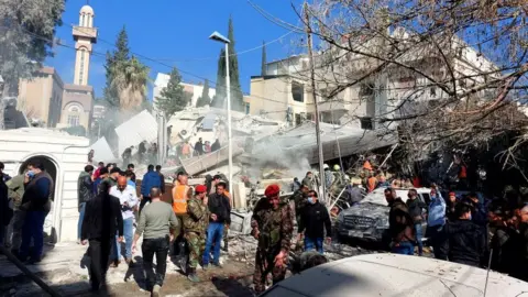Getty Images People and security forces gather in front of a building destroyed in an explosion in Damascus on Saturday