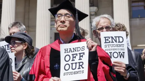 Professor in cap and gown holding sign