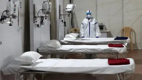 Reuters A woman wearing a protective suit stands next to beds inside a hospital that has been constructed to treat patients who test positive for the coronavirus disease (COVID-19),
