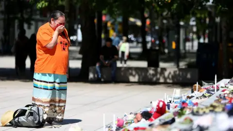 Getty Images A woman mourns over 215 pairs of children's shoes outside Vancouver Art Gallery.