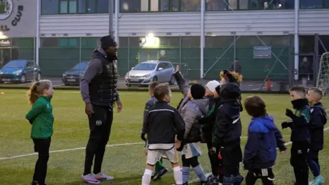 Man chats to group of children on football pitch