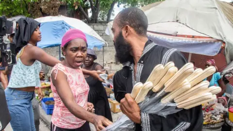 Getty Images Community leader Nertil Marcelin (30) distributes machetes to residents as he initiates a plan to resist gangs and take over their neighborhoods in the Delmas district of Port-au-Prince, Haiti on May 16, 2023.