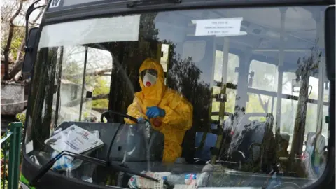 Getty Images A man (in yellow) dressed in protective gear drives a special service bus taking people to a quarantine facility amid concerns about the spread of the COVID-19 coronavirus in Nizamuddin area of New Delhi on March 31, 2020