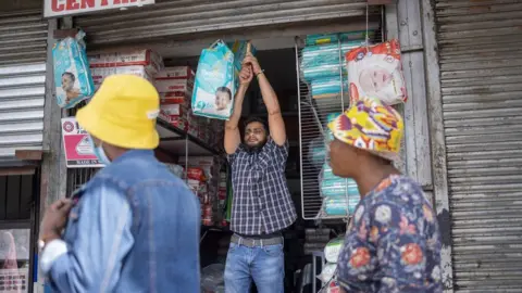 AFP Shutters are closed as disgruntled South African job seekers belonging to the anti-foreigners movement called "Operation Dudula" sing slogans and dance while marching through Alexandra township, on March 7, 2022.