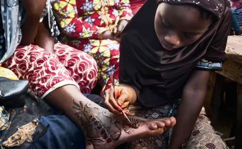 AFP A girl painting henna on to a woman's foot in Bamako, Mali - Monday 20 August 2018