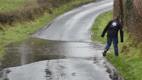 Pacemaker A pedestrian walks on grass verge to avoid flood