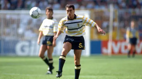 Getty Images Scotland players wearing white shirts with blue and yellow hoops, blue shorts and blue socks during the 1990 World Cup.
