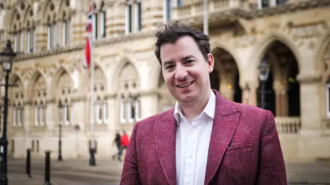 Office of Mike Reader Labour MP Mike Reader in front of the Guildhall, Northampton wearing a burgundy jacket and white shirt