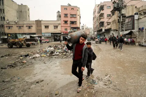 Reuters A young boy walks through a street in Gaza City on 3 February while carrying a tank of water