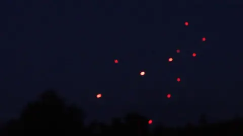 MOOSE CAMPBELL/BBC Tracer fire - which looks like eleven small red dots - can be seen amongst pitch black sky. Tree tops are just about visible in the darkness.