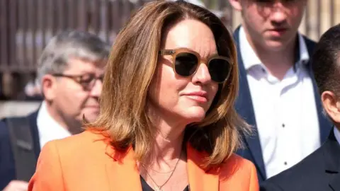 Woman in sunglasses with orange blazer.