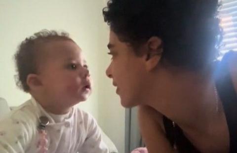 Baby Orla, wearing a white baby grow, face to face with Olayka, who is wearing a black vest top