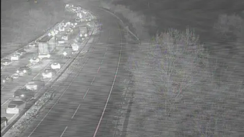 Black and white image of vehicles queuing on the A14. It is dark and the vehicles have their lights on.