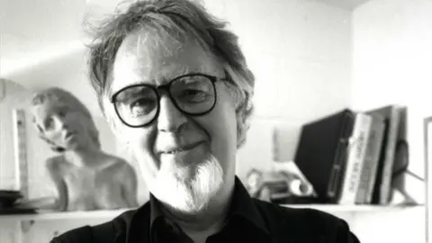 MANX NATIONAL HERITAGE A black and white photo of Bryan Kneale, who have dark hair and grey beard and  black rimmed glasses.