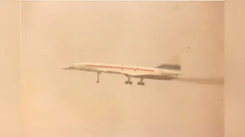 The Concorde prototype is seen taking off into the air. It is white with a red and a blue stripe.