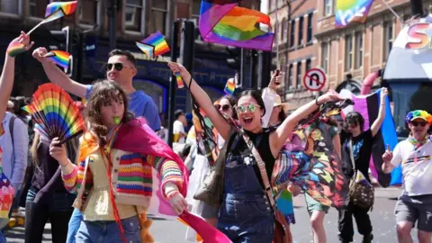 PA Media A group of people waving rainbow LGBTQ+ flags.