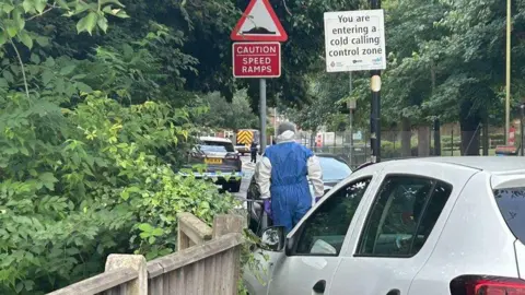 SWNS A forensic investigator walks down the street with his back to the camera in the Sally Port Gardens area