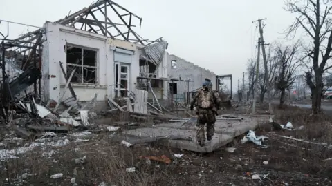 EPA-EFE/REX/Shutterstock A Ukranian soldier walks near a home destroyed by Russian troops in Lypsi, located on the Kharkiv front line, Kharkiv, Ukraine, 27 January 2025. 