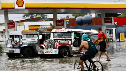 EPA People wade to access a submerged gasoline station in Meycauayan, Bulacan, Philippines