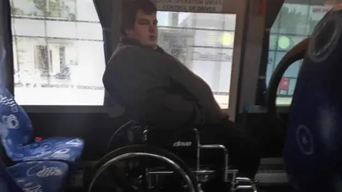 Charley Jonstone-Brent Charley Jonstone-Brent who uses a mobility aid, sat in a wheelchair on a coach.  