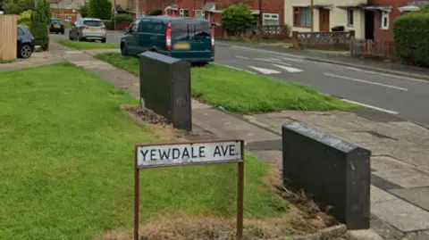 A street view of the road. There is a green verge and the road sign reads: 'YEWDALE AVE'.