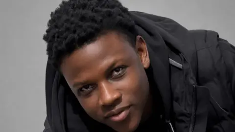 Supplied Panashe is smiling towards the camera and is wearing a black hoodie. He has short black hair. 