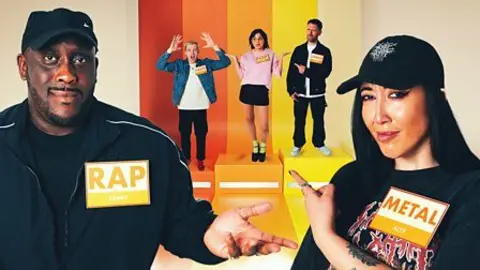 Two Radio 1 DJs, Kenny Allstar and Alyx Holcombe, point at three others standing on a podium behind them