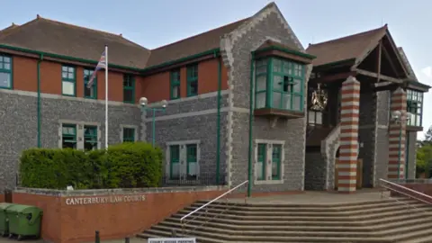 outside Canterbury Crown Court, a grey stone building with two pitched roofs and two striped red brick columns at the entrance