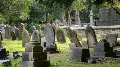 Historic England A number of stone monuments and gravestones, some of which are leaning forwards 