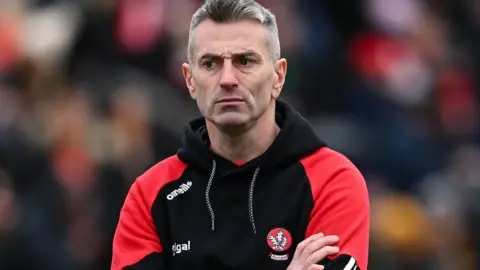 Getty Images A man in a black Derry GAA hoodie with red sleeves is looking slightly off-camera. He has short grey hair. He is standing in front of a blurred background that appears to be of a large crowd at a sporting event.