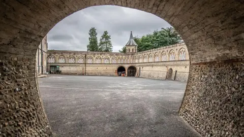 A photo taken from just inside the entrance of a tunnel, looking out at the courtyard of a grand looking building. 