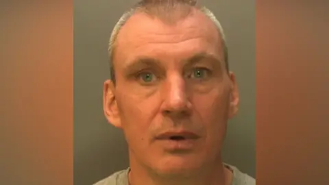 A bald man with grey shaved hair. 
