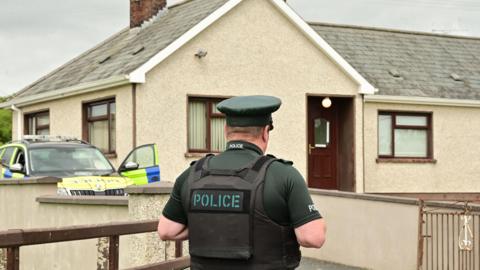 A PSNI officer stands with his back to the camera in front of a house where Michael McConville was found in Crossmaglen