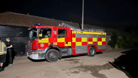 Dean Elcome/Natural England A fire engine parked in front of a black farm building. Two men are standing next to it. 