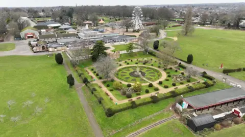 Stephen Huntley/BBC An aerial view of Wicksteed Park with ornamental garden and miniature railway track and station in the foreground. A big wheel and other buildings and rides are in the background, with grassy areas either side.