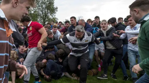 Getty Images Men in a field grappling to grab a beer barrel. 