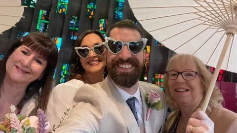 Four people in a selfie, the man and woman in the centre are wearing We Still Do sunglasses