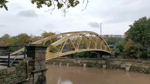 Bristol City Council Langton Street Bridge in Bristol. It is yellow metal bridge spanning the river.
