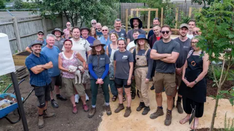 A group of people in gardening gear stand in a newly created community garden. 
