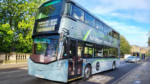 A large silver double decker bus with the X23 on the front crosses Magdalen Bridge.