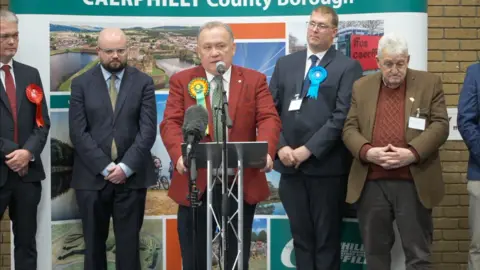 Lindsay Whittle in a red blazer on a stage with four other candidates behind him